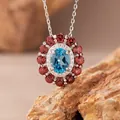 Detaillierte Makroansicht des ovalen blauen Topas-Anhängers mit rotem Granat-Heiligenschein - Halskette / Natürlicher Topas / Blau