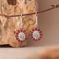 Detaillierte Nahaufnahme von blumenförmigen Aquamarin- und Granat-Ohrhängern am Zweig - Ohrstecker / Natürlicher Aquamarin / Hellblau