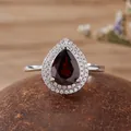 Close-up detail of a pear-shaped dark red gemstone ring with a double halo of sparkling clear stones - Garnet