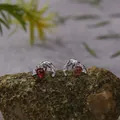 Close-up of S925 silver stud earrings with red garnet stones on a textured rock - Garnet Stud Earrings / Silver