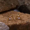 Detailed close-up view of gold organic arch stud earrings featuring round white pearls - Pearl Stud Earrings / Gold