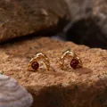 Macro view of gold-plated sterling silver earrings with deep red garnet stones - Garnet Stud Earrings / Gold