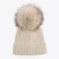 Detailed macro view of the soft ribbed texture and fluffy faux fur pom-pom on beanie - Light Beige