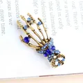 Vintage skeleton hand brooch with vibrant blue rhinestones on a book background. - Dark Blue