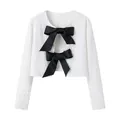 Detail view of a white sequined cropped jacket featuring two large black satin bows on the front. - XS / Tops / White