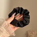 Mano sosteniendo un elegante coletero de satén negro de gran tamaño con brillo. - 10cm / Negro Brillante