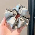 Mano que sostiene un coletero gigante de satén gris plata con acabado sedoso - 11cm / Verde Cardamomo