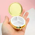 Portable mini golden metal pill box with three compartments shown open in hand - 60mm Round Push-Button Pill Box 3 Compartments / Gold