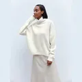 Model wearing a soft ivory white high turtleneck sweater with ribbed knit details - White