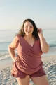 Close-up of a plus-size mauve sleeveless romper with ruffle hem details on a sunny beach. - Brick Red