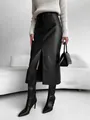 Front slit detail of stylish high-waisted black faux leather midi skirt worn by model - S / Bottoms / Black