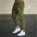 Detail shot of men's olive green slim-fit drawstring joggers featuring a small crown logo accent - M / Bottoms / Green