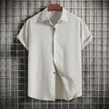 Macro view of cream-colored textured short-sleeved button-up shirt hanging on wooden hanger. - Off White