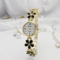 Close-up of gold-tone flower bracelet watch with black enamel petals and white dial - Gold Black