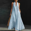 Full-length view of a woman in a light blue linen halter dress holding a straw bag - Sky Blue