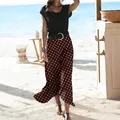 Lifestyle detail of a brown polka-dot midi skirt worn by a woman on a sunny beach - S / Bottoms / Coffee