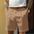 Detail of men's khaki pleated linen shorts with stylish cuff and brown leather belt. - Caramel color