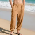 Detailed view of men's loose breathable cotton linen casual pants with drawstring on a beach - Caramel color