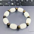 Detailed shot of a white and black beaded bracelet with gold mantra engravings - PiXiu Luck Bracelet / White Jade Look and Mantra