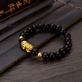 Detailed view of a black obsidian style bracelet with a gold Pixiu charm on a dark wooden desk - Golden Beads PiXiu Bracelet / 8mm
