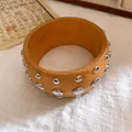 Detaillierte Nahaufnahme eines Vintage Holzarmreifens mit silbernen Metallnieten auf Leinen - Bernstein Silber Nieten Dekoration / Beige-Silber