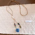 Detailed view of handmade ceramic rose and leaf pendant on adjustable leather cord. - Blue