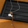 Close-up view of a silver fish pendant necklace with a leather cord on a black tray. - Small Fish Pendant / Silver and Coffee