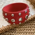 Close-up of a red wooden bangle with polished silver-tone rivets on woven texture. - Silver-Red