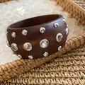 Detailed view of a wide dark brown wooden bangle embellished with shiny silver rivet studs. - Silver-Brown