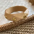 Detailed view of an irregular geometric wooden bangle featuring gold studs on a woven surface. - Creamy Yellow