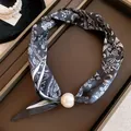 Close-up van een zwarte zijden sjaalketting met paisley-print en grote parel magneetsluiting - Zwart Paisley Stijl / Zwart