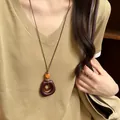 Detailed shot of a vintage brown wooden circular pendant necklace worn over a khaki top - Irregular Nested Resin Style (76#) / Coffee