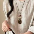 Dettaglio di una collana etnica con pendente in pietra occhio di tigre su camicia di lino - Goccia Occhio di Tigre (25#)