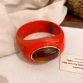 Nahaufnahme eines roten Acryl-Armreifs mit einem ovalen Bernstein-Harz-Element. - Armreif / Rot-Kaffee