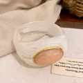 Detailaufnahme eines Retro-Acrylarmreifs mit marmoriertem rosa Oval und Goldrand - Armreif / Weiß-Rosa