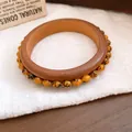 Detailaufnahme von Retro-Holzarmreif und orangefarbenem Perlenarmband auf Leinen. - Retro Muster Ethno Armband / Kaffee-Gelbe Schwarze Musterperlen