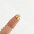 Makroansicht der winzigen 18K vergoldeten Edelstahl-Blütenperle auf einer Fingerspitze - Wellenring-Stil (1#)