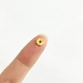 Makroaufnahme einer vergoldeten Edelstahl-Blumenzwischenperle auf einer Fingerspitze - Stereo Sechsblättrige Blume Stil (2#)