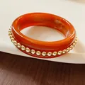 Detail of an orange resin bangle accented with small gold spheres on white tray - Metal Beads / Brown