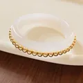 Close-up of a minimalist white resin bangle accented with polished golden metal beads - Metal Beads / White