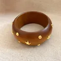 Detailansicht eines hölzernen Armreifs mit goldfarbenen Sternen und Nieten-Verzierungen. - Goldene Pentagramm Nieten Dekoration / Dark Brown And Gold