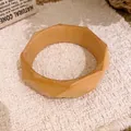Nahaufnahme eines minimalistischen facettierten Holzarmreifs auf rustikalem Hintergrund - Geometrisch Facettierte Holzfarbe / Khaki-Holzfarbe