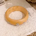Nahaufnahme eines hochwertigen Holzarmreifens mit eingebetteten silbernen Metallnieten - Industrielles Retro Breites Niete / Hellbraun-Silberne Nieten