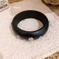 Nahaufnahme eines schwarzen Holzarmreifs mit silbernen Nietendetails auf gewebter Fläche - Schwarzes Breites Armband Silbernieten / Schwarz Mit Silbernen Nieten