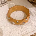 Nahaufnahme eines facettierten Holzarmbands mit runden und rautenförmigen Metallnieten - Polyeder Facettierte Bräunung Niete / Khaki-Silberne Nieten