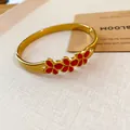 Close-up detail of a vintage gold bangle featuring three vibrant red enamel flowers. - Enamel Flower Style / Gold-Red