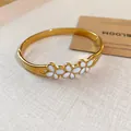 Close-up detail of vintage gold bangle featuring elegant white enamel floral motifs on a textured surface - Enamel Flower Style / Gold-White
