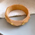 Detailaufnahme eines facettierten Holzarmreifs mit goldenen Nieten auf neutralem Grund - Geometrisches Polyeder Rautenmuster / Naturholzfarbe