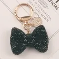Close-up of black rhinestone bow keychain with elegant gold hardware and tag. - Black