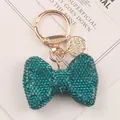 Detailed close-up of a sparkling teal rhinestone bow keychain with elegant gold hardware. - Blue